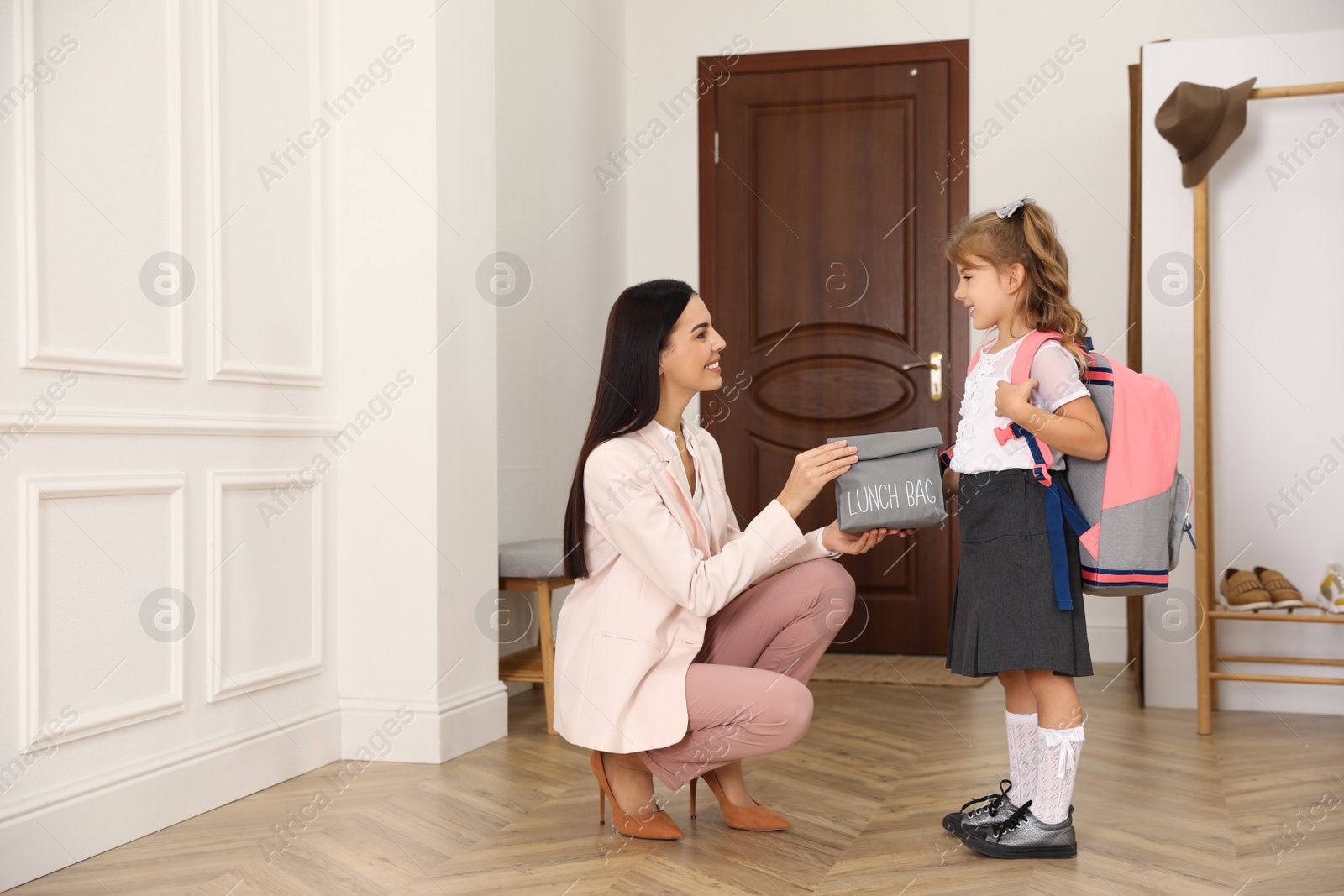 Photo of Mother helping her little child get ready for school in hallway