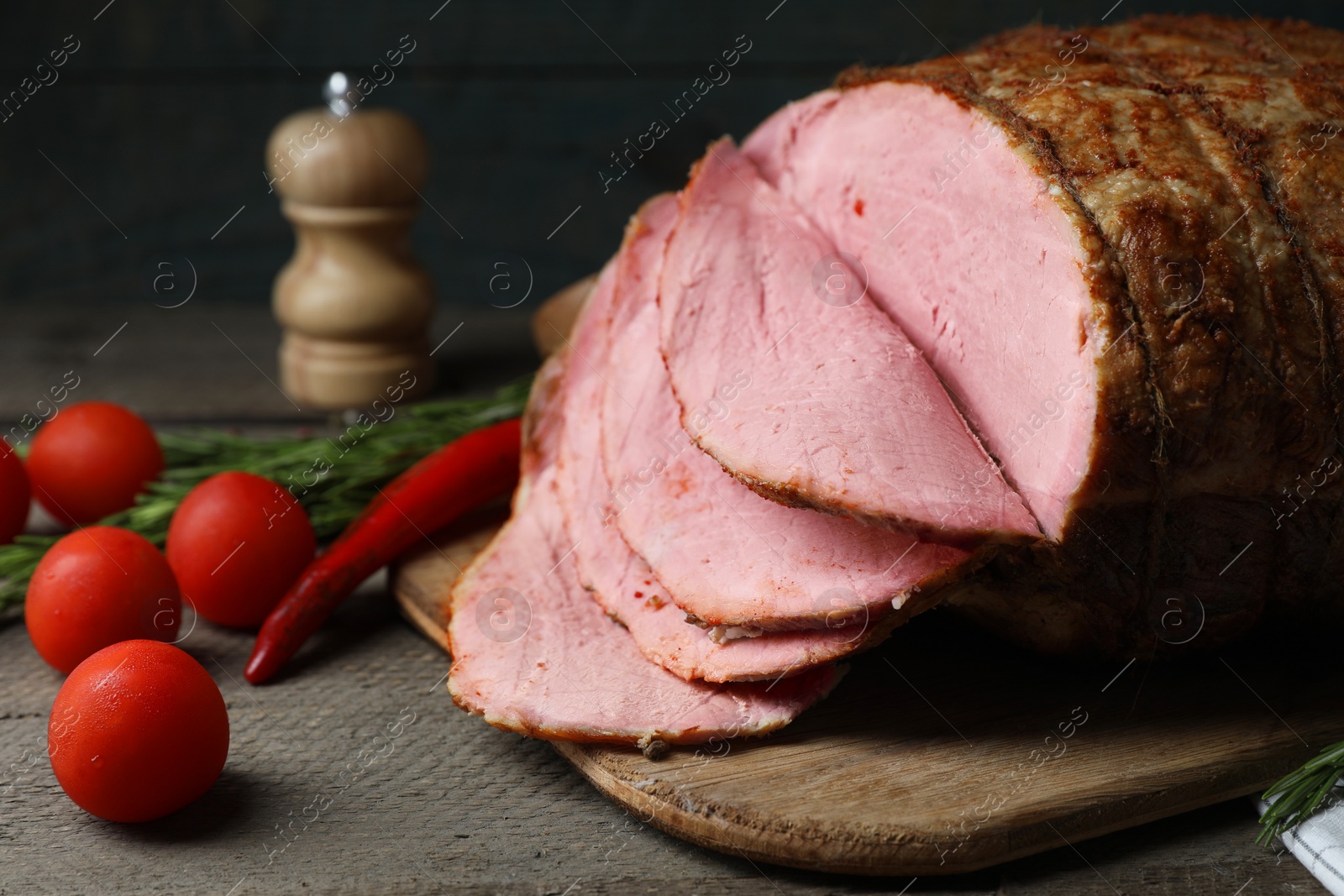 Photo of Delicious baked ham, tomatoes, chili pepper and rosemary on grey wooden table, closeup