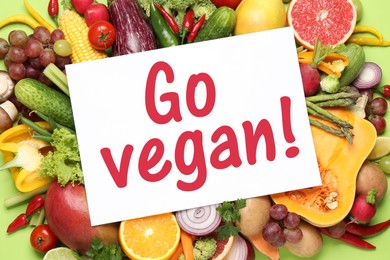 Image of Paper card with phrase Go Vegan, fresh vegetables and fruits on green background, top view