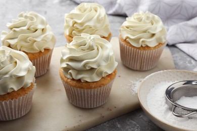 Photo of Tasty cupcakes with vanilla cream on grey table, closeup