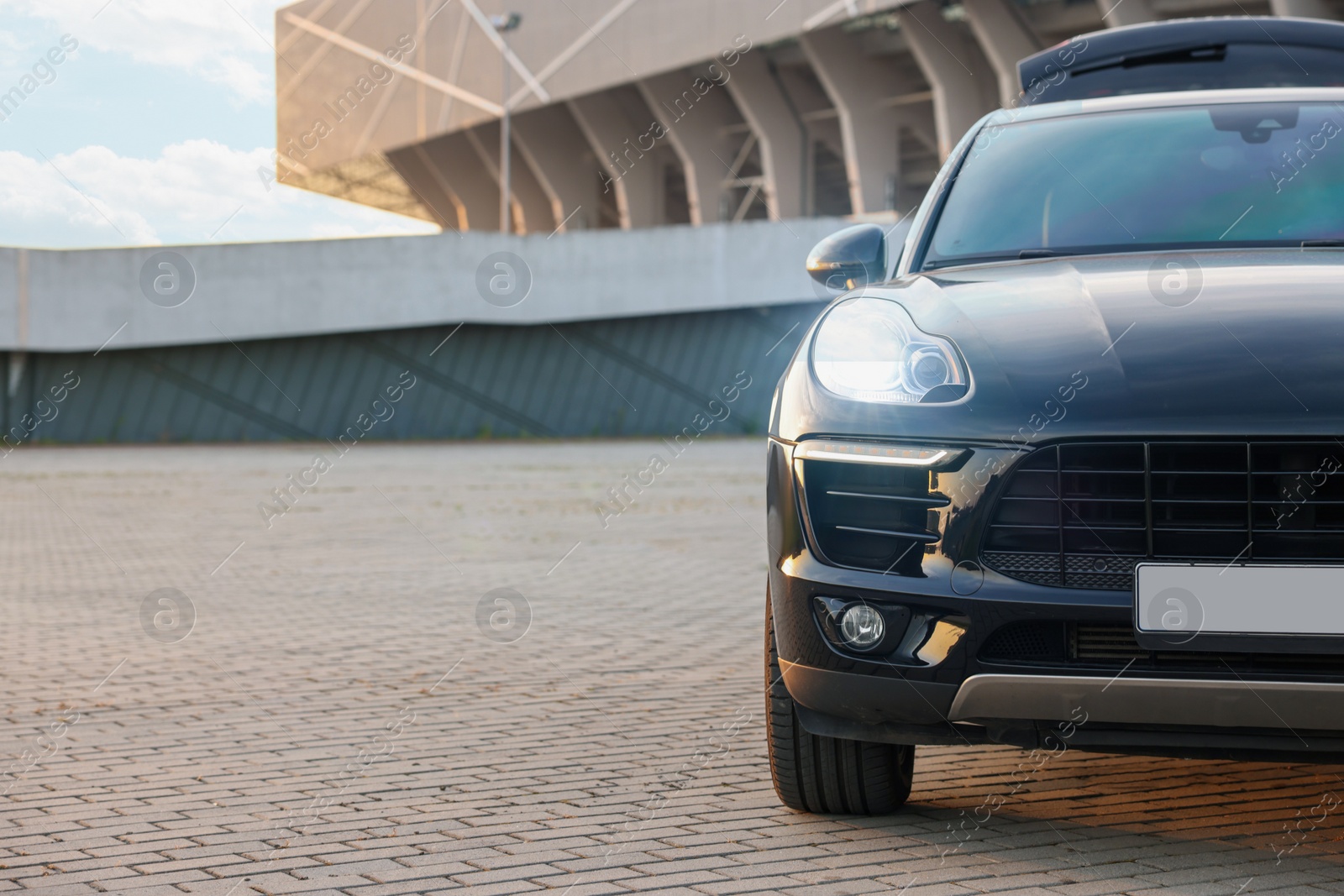 Photo of Modern black car parked on stone pavement outdoors, space for text