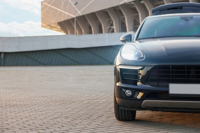 Modern black car parked on stone pavement outdoors, space for text