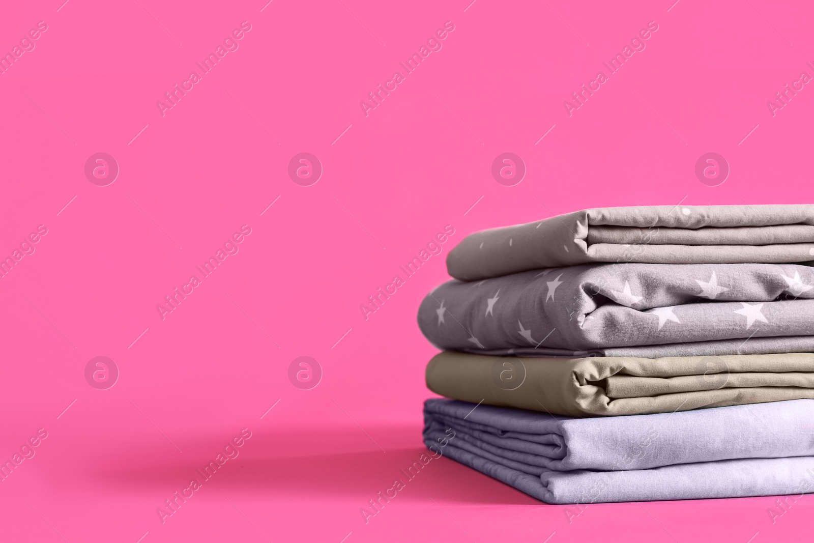 Photo of Stack of clean bed sheets on pink background. Space for text