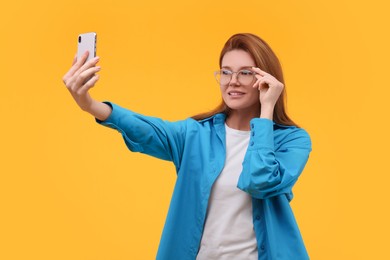 Beautiful woman in eyeglasses taking selfie on orange background