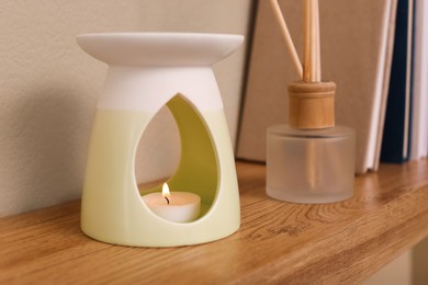 Photo of Stylish aroma lamp and reed diffuser on wooden shelf indoors