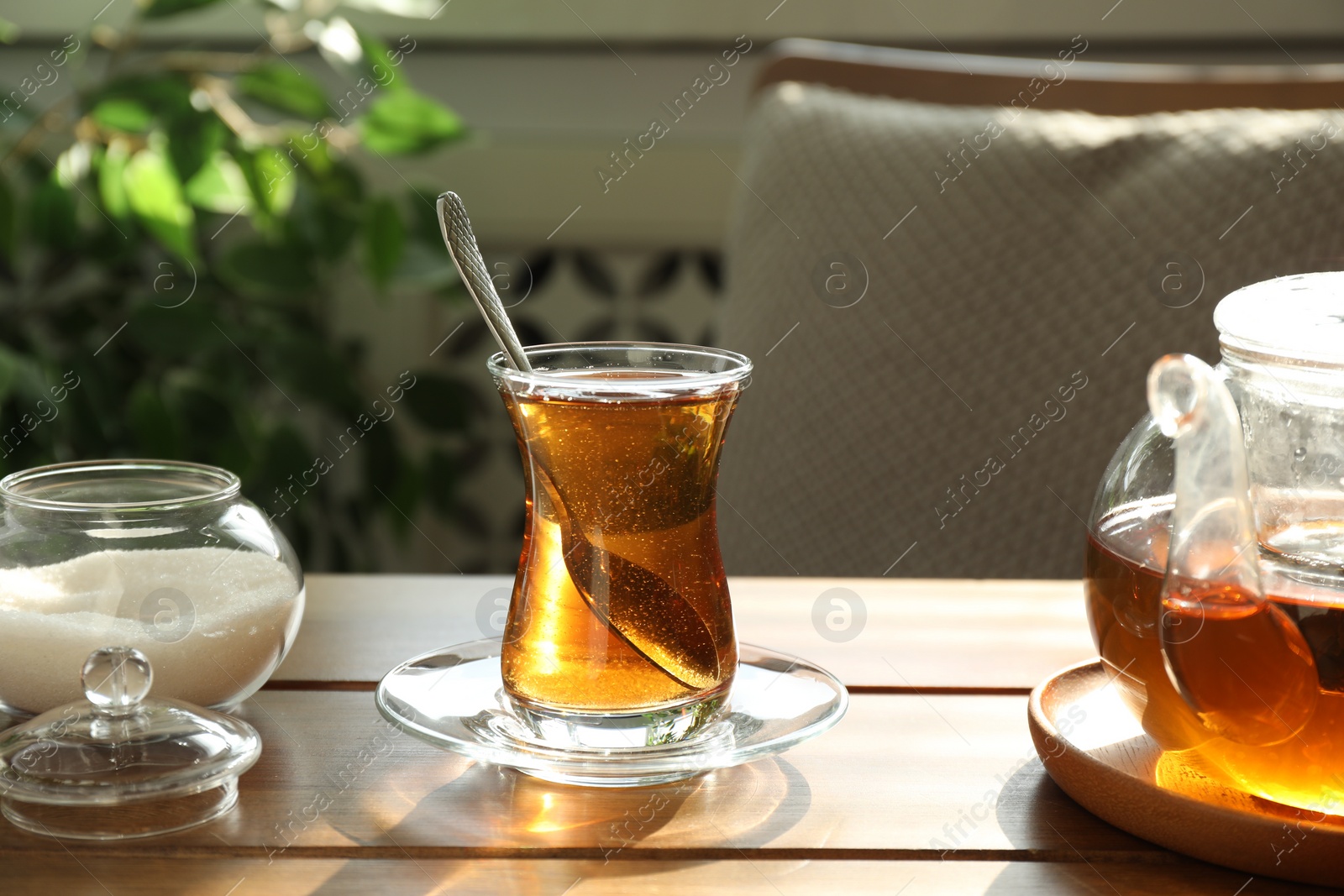 Photo of Aromatic tea in glass, teapot and sugar on wooden table indoors