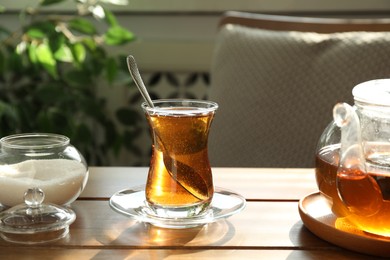 Aromatic tea in glass, teapot and sugar on wooden table indoors
