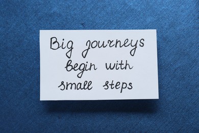 Photo of Card with phrase Big Journeys Begin With Small Steps on blue background, top view. Motivational quote