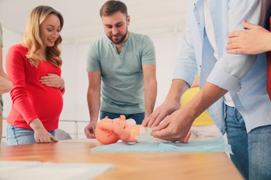 Photo of Future fathers and pregnant women learning how to swaddle baby at courses for expectant parents indoors, closeup