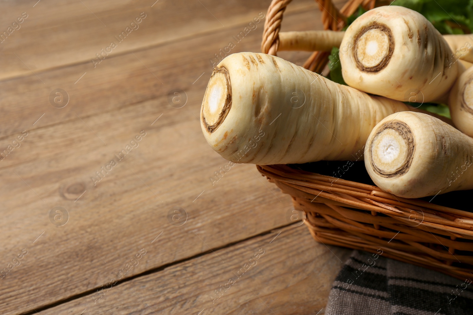 Photo of Wicker basket with delicious fresh ripe parsnips on wooden table, closeup. Space for text