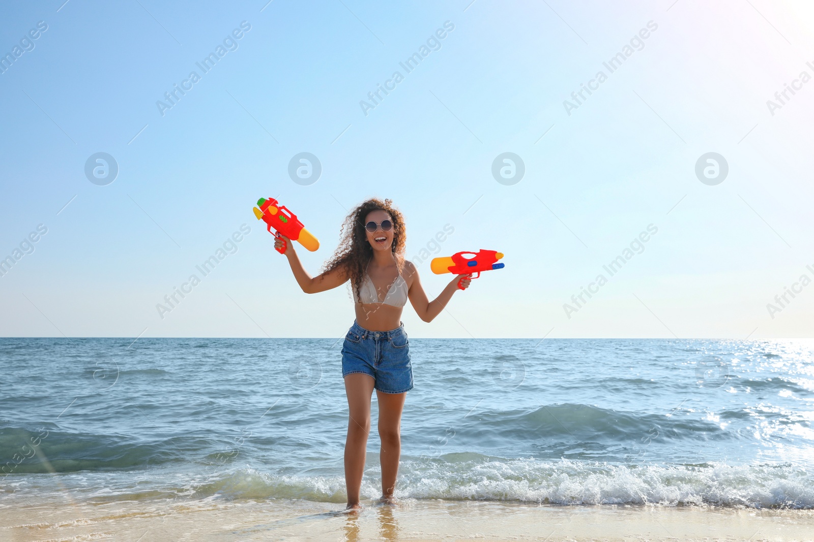 Photo of African American woman with water guns having fun on beach