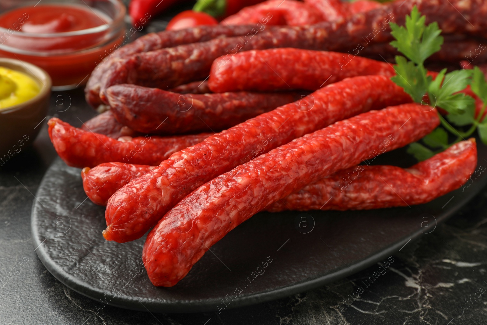 Photo of Thin dry smoked sausages served on black marble table, closeup