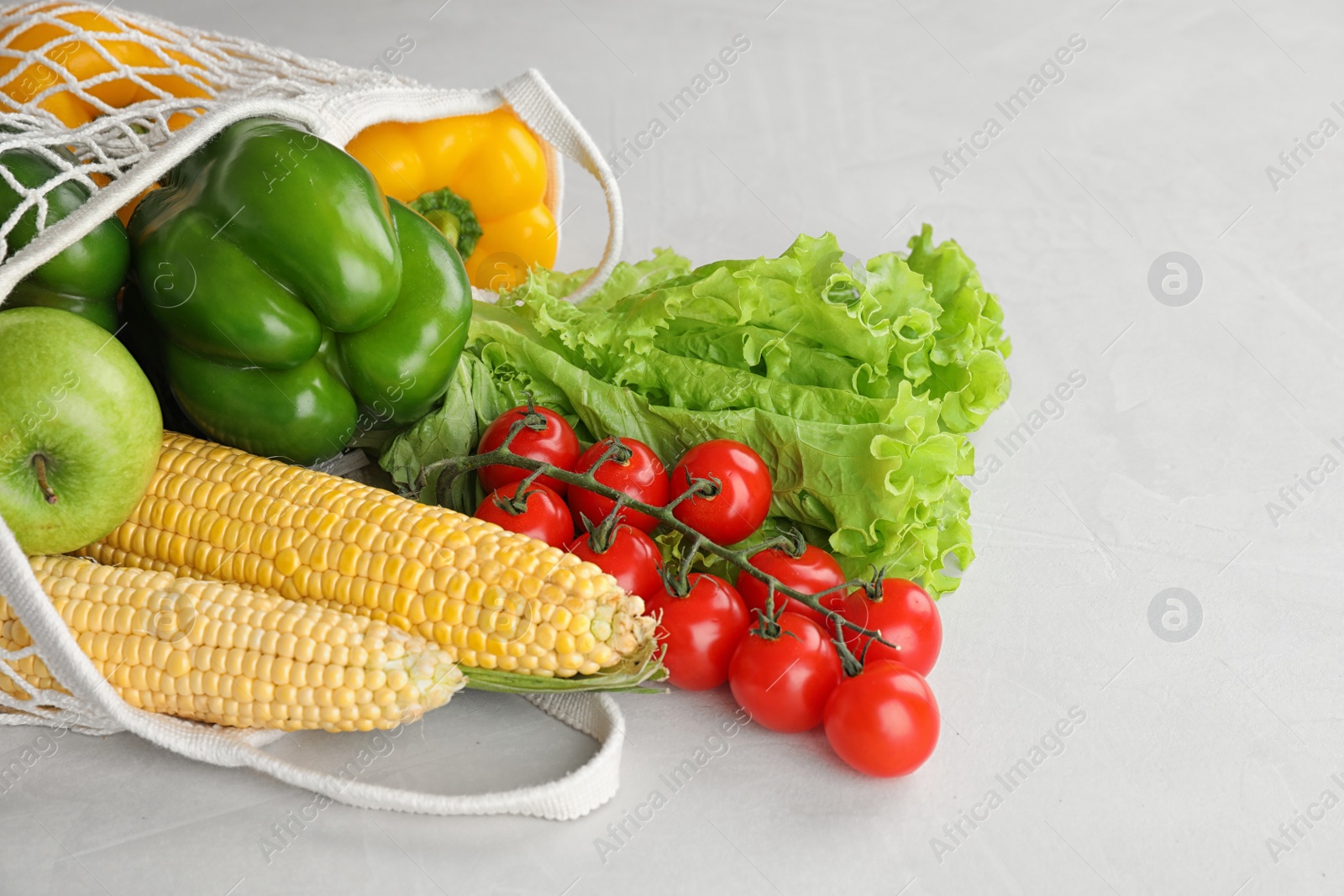 Photo of Different fresh vegetables and fruits in mesh bag on light table