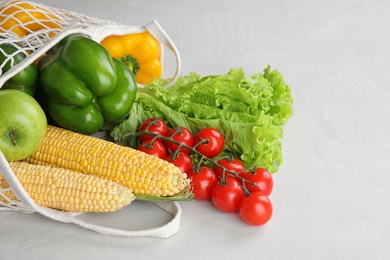 Photo of Different fresh vegetables and fruits in mesh bag on light table