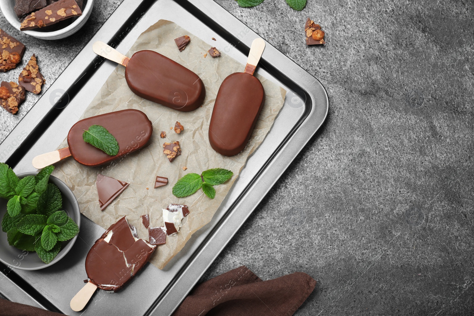 Photo of Flat lay composition with glazed ice cream bars, fresh mint and chocolate on grey table. Space for text