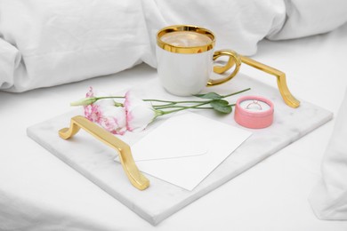 Photo of Tray with cup of coffee, flowers and beautiful engagement ring in box on white bed