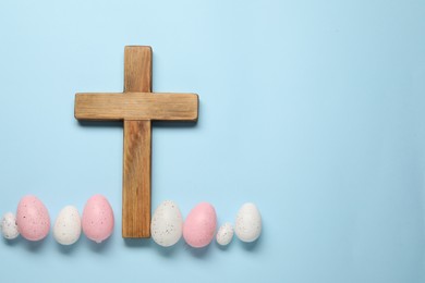 Photo of Wooden cross and painted Easter eggs on light blue background, flat lay. Space for text