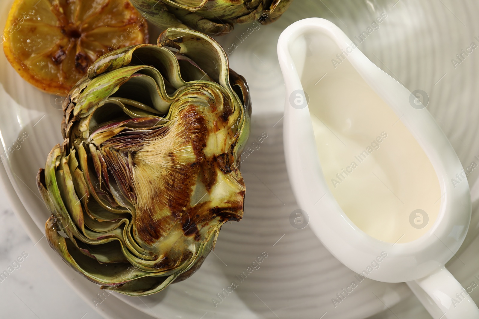 Photo of Tasty grilled artichokes, lemon and sauce on table, top view