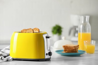 Photo of Yellow toaster with roasted bread slices and orange juice on white marble table