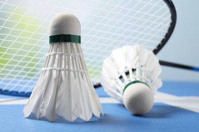 Feather badminton shuttlecocks and racket on blue table against blurred background, closeup
