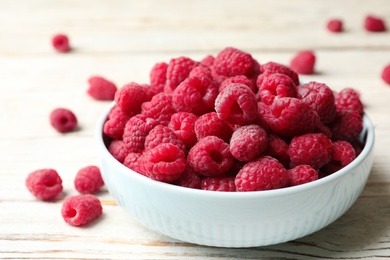 Photo of Bowl of delicious fresh ripe raspberries on white wooden table, closeup view