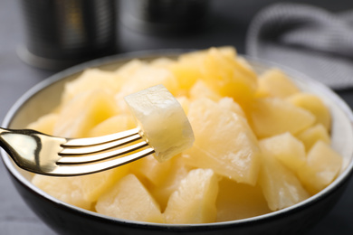 Photo of Fork with canned pineapple piece over bowl, closeup