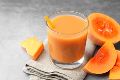 Photo of Tasty pumpkin juice in glass and cut pumpkin on light grey table