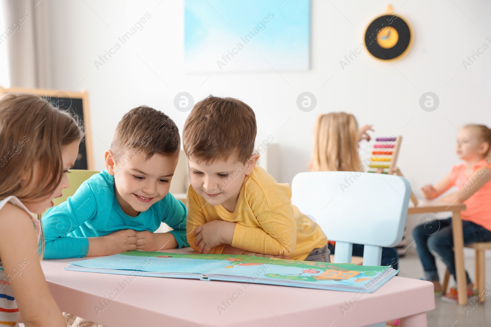 Photo of Cute little children reading book at table indoors. Learning and playing