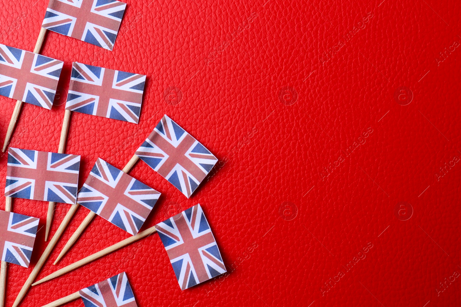 Photo of Small paper flags of United Kingdom on red textured background, flat lay. Space for text