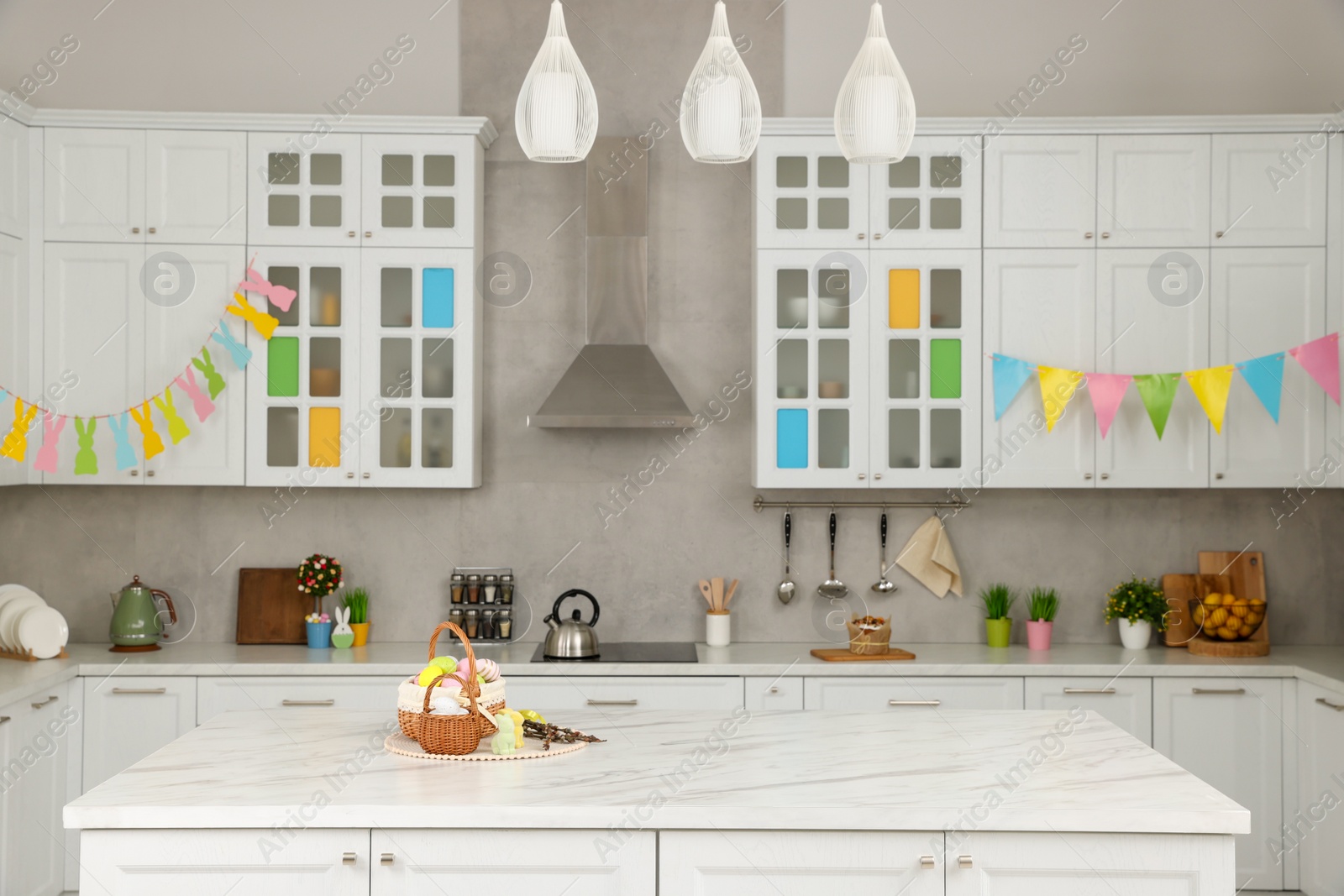 Photo of Wicker baskets with Easter eggs at white marble table and festive decor in kitchen