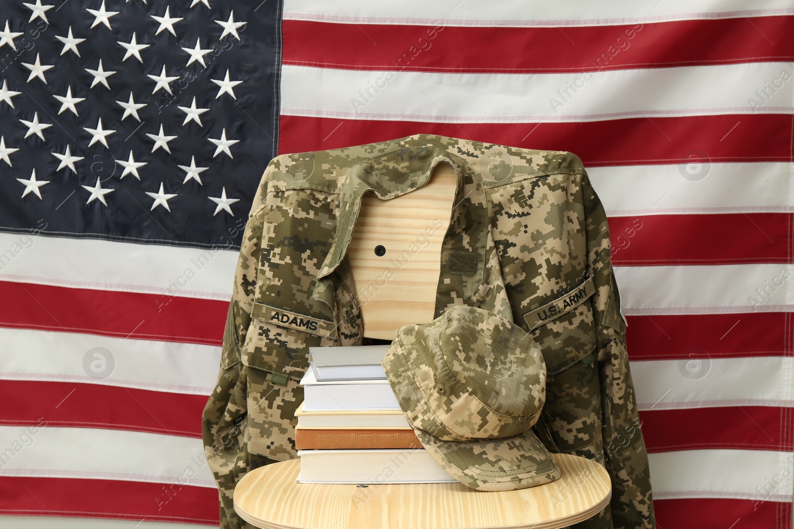 Photo of Books and soldier uniform on wooden chair near flag of United States. Military education