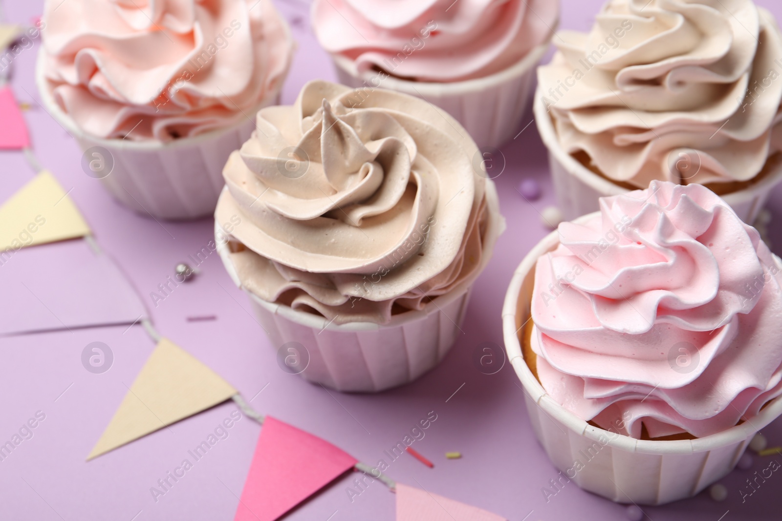 Photo of Delicious birthday cupcakes, sprinkles and bunting flags on violet background, closeup