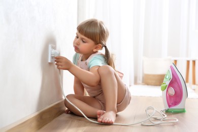 Little child playing with electrical socket and iron plug at home. Dangerous situation