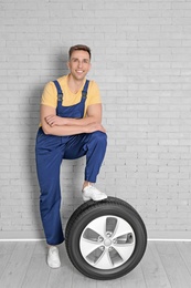 Male mechanic with car tire on brick wall background