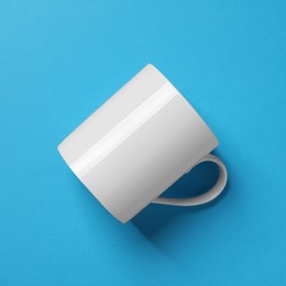 Photo of One white ceramic mug on light blue background, top view