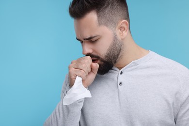 Photo of Sick man with tissue coughing on light blue background, space for text