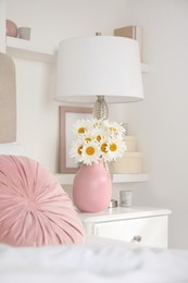 Bouquet of beautiful daisy flowers and lamp on nightstand in bedroom