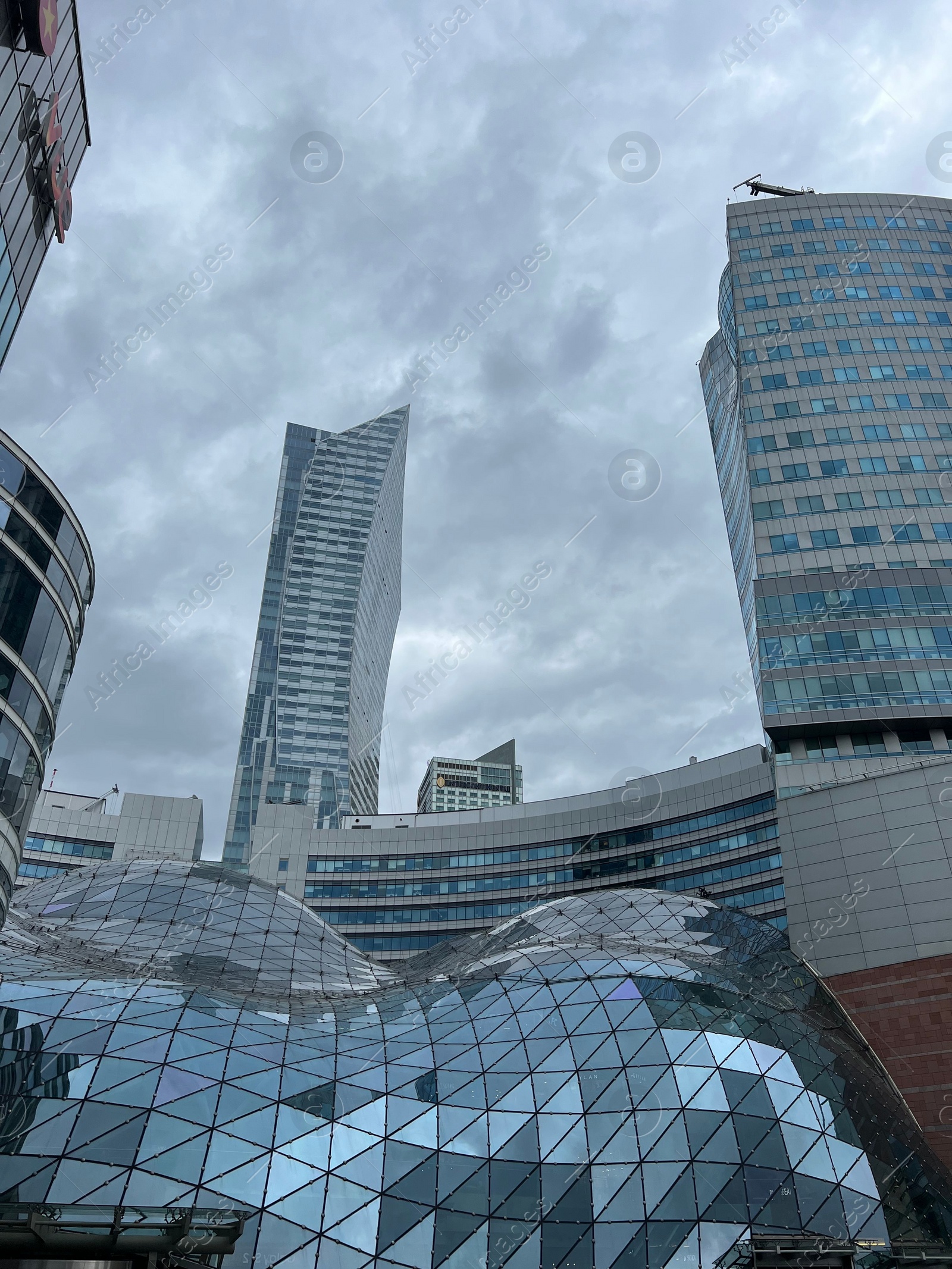 Photo of WARSAW, POLAND - JULY 17, 2022: Big shopping mall and buildings under cloudy sky, low angle view