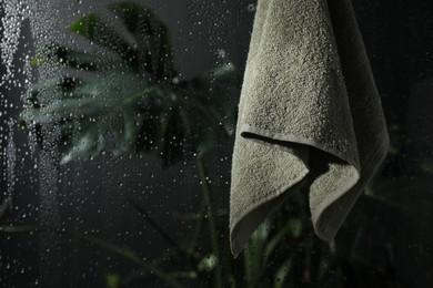 Photo of Terry towel hanging on wet glass wall in shower, space for text