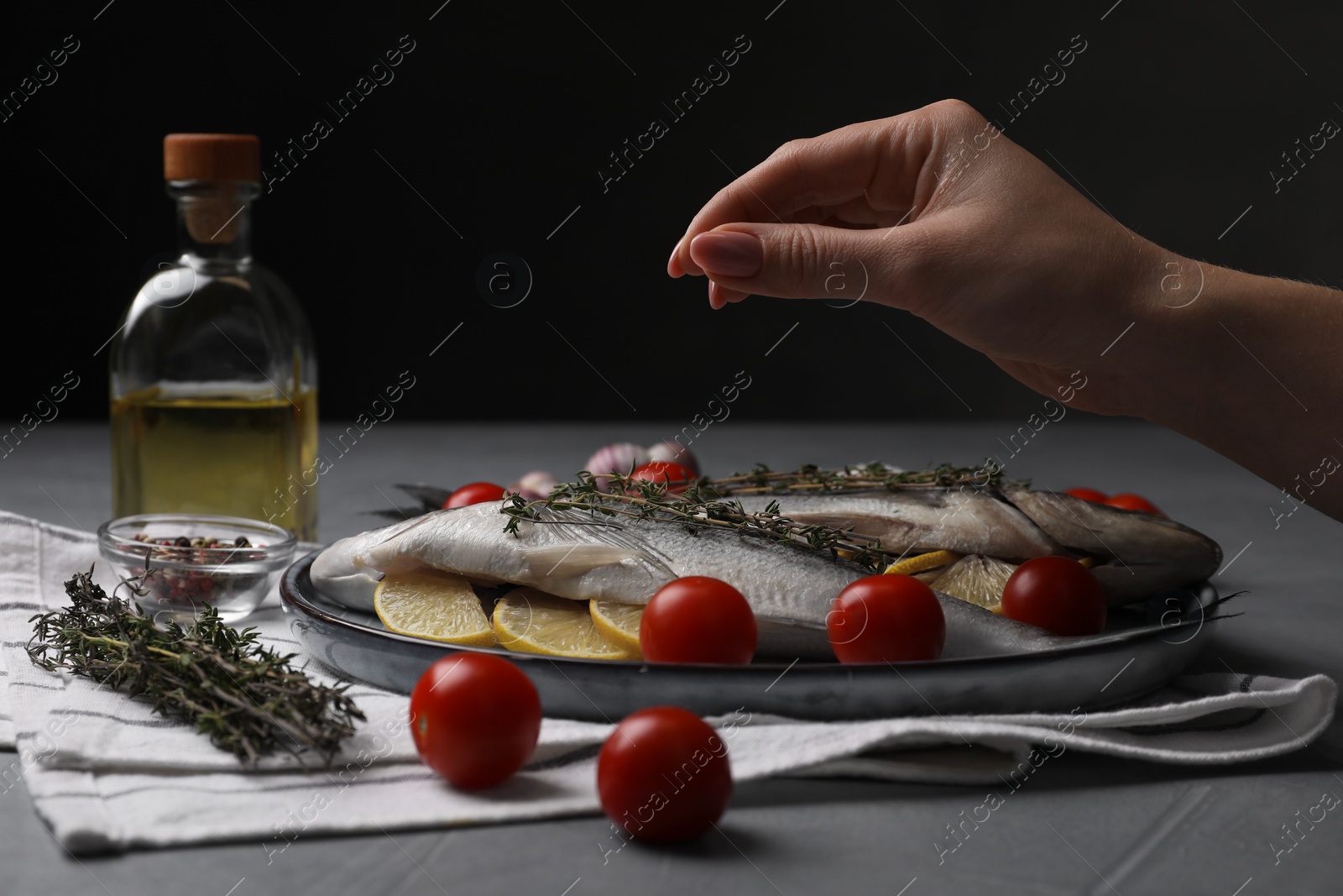 Photo of Woman salting raw dorado fish at grey table, closeup