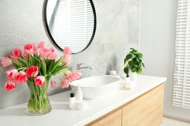 Vase with beautiful pink tulips and toiletries near sink in bathroom