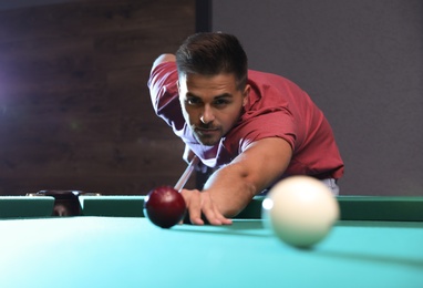 Handsome young man playing Russian billiard indoors