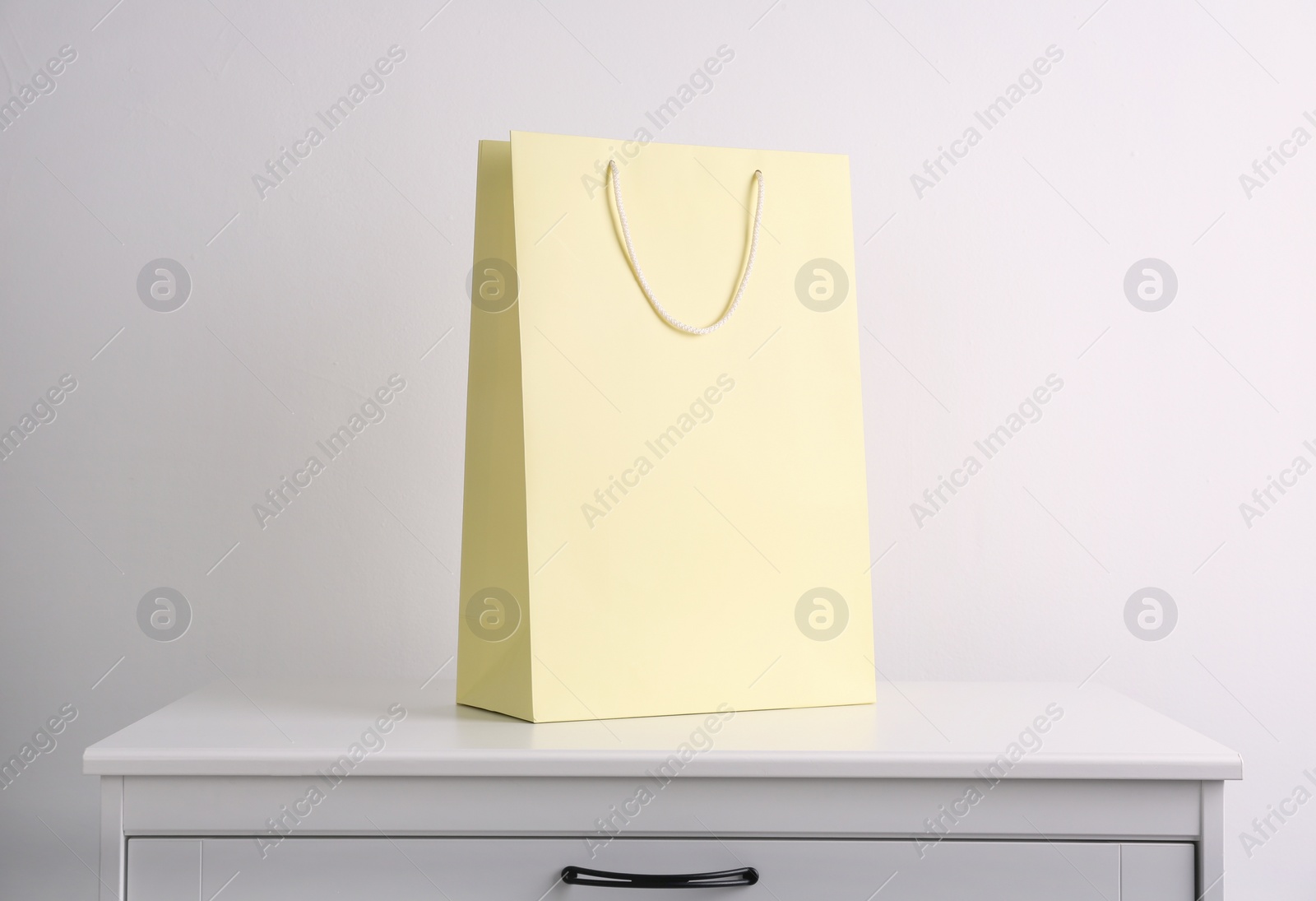 Photo of Paper shopping bag on white chest of drawers against light background
