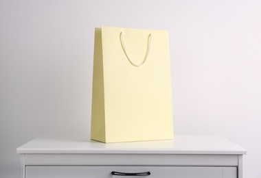 Photo of Paper shopping bag on white chest of drawers against light background
