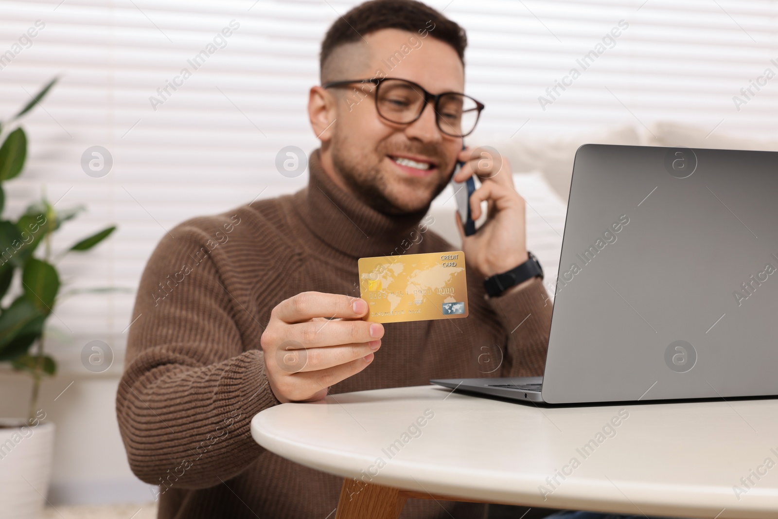 Photo of Handsome man with credit card using smartphone and laptop for online shopping at home, selective focus