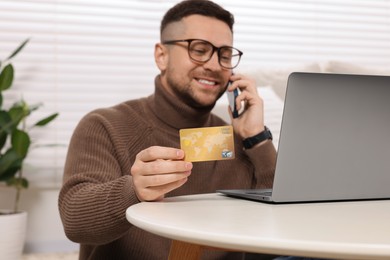 Handsome man with credit card using smartphone and laptop for online shopping at home, selective focus