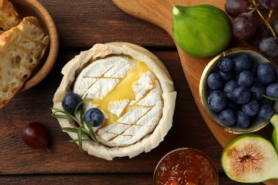 Photo of Tasty baked brie cheese and products on wooden table, flat lay