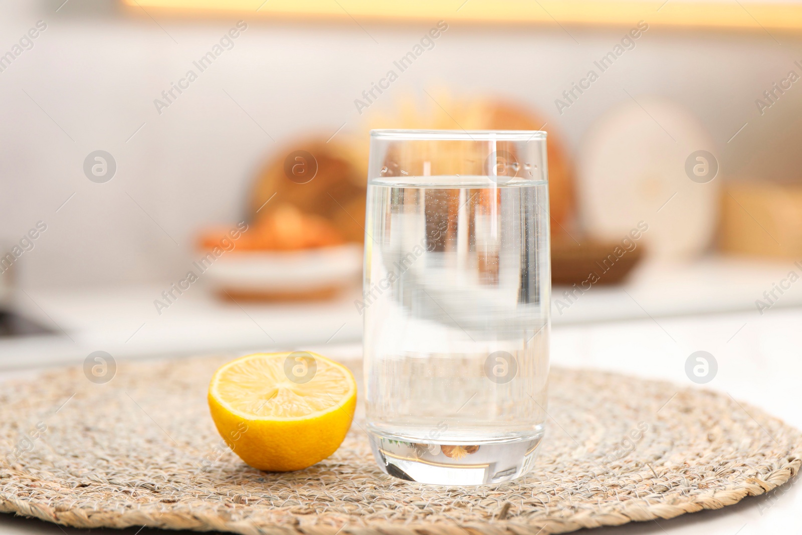 Photo of Glass with clear water and half of lemon on table in kitchen