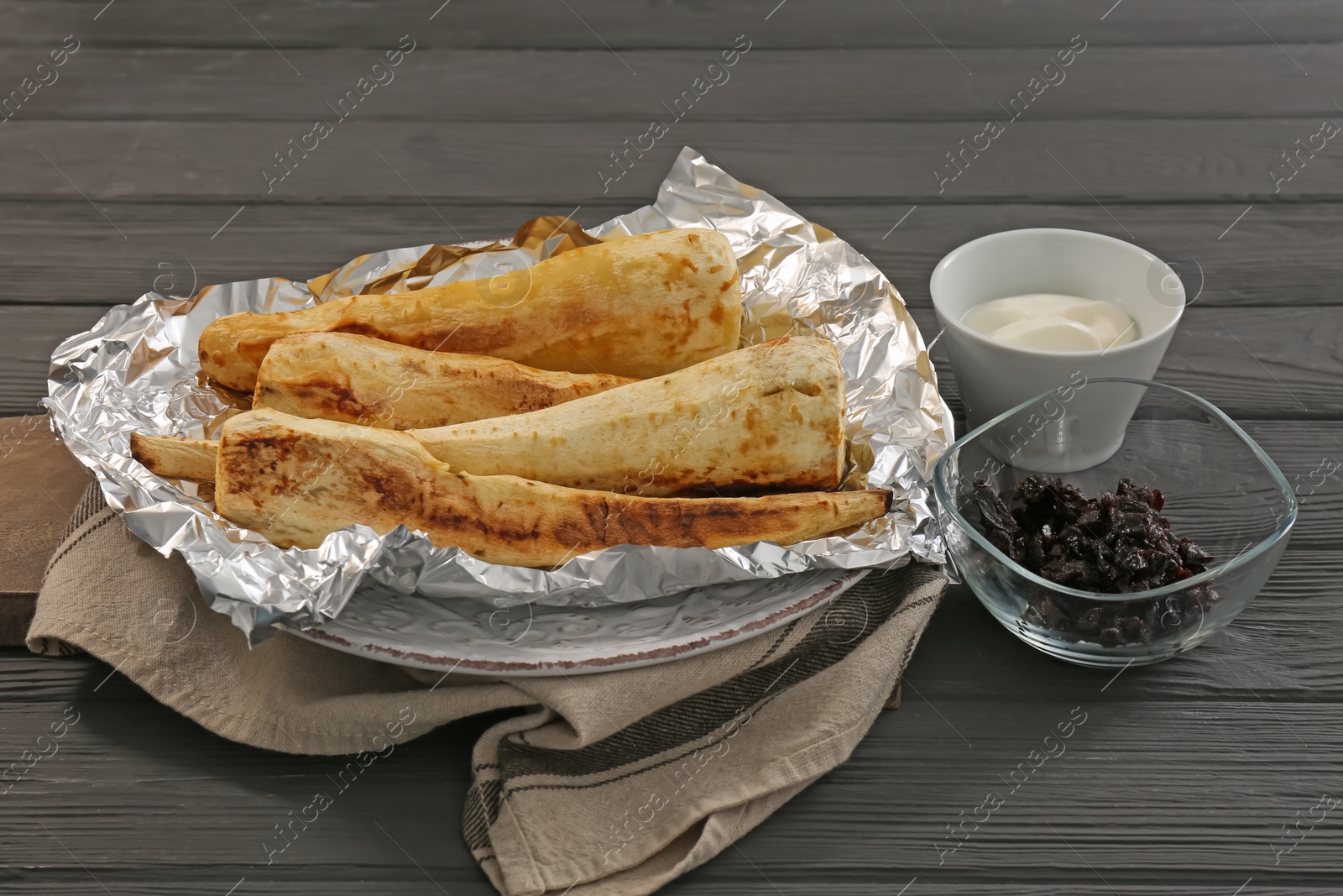 Photo of Tasty baked parsnips, prunes and sauce on dark wooden table