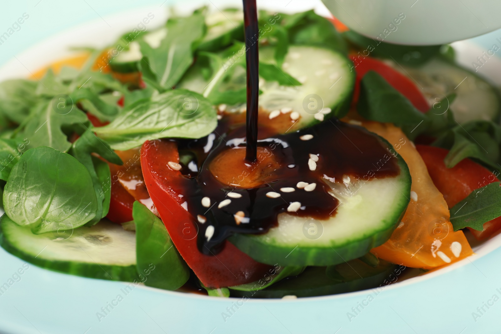 Photo of Pouring balsamic vinegar onto fresh vegetable salad in dish, closeup